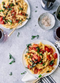 蓝色的桌子上放着两盘白色的沙拉，上面有西红柿、罗勒和意大利面，还有一杯葡萄酒。