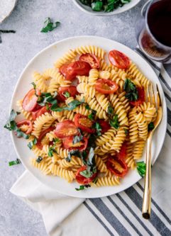 一个白色板与冷意大利通心粉沙拉fusilli pasta, tomatoes, and basil with a gold fork.