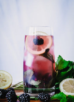 一杯充满酒精的黑莓柠檬水放在砧板上，上面放着新鲜的水果。