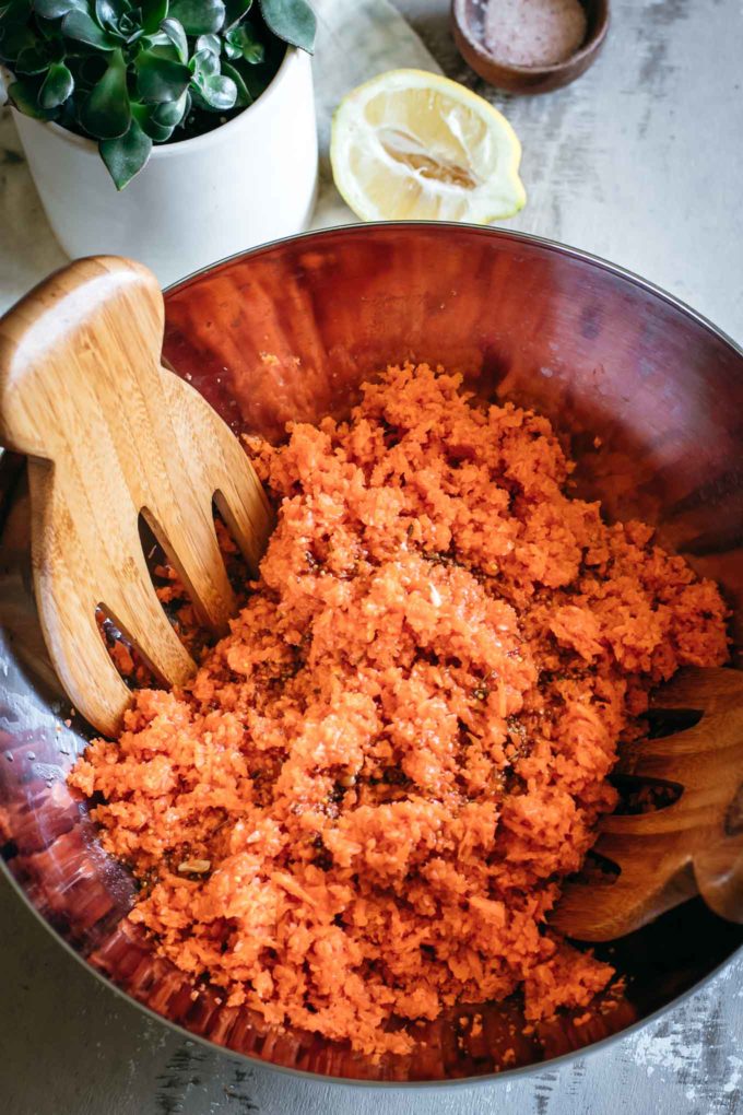 切碎的胡萝卜和敷料在一个大搅拌碗里用木勺