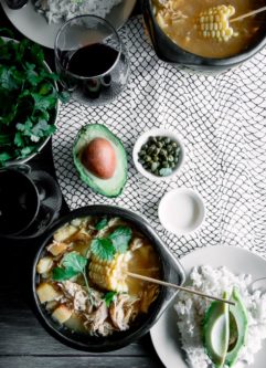 chamba锅与哥伦比亚阿吉亚科（Ajiaco）一起放在木桌上，上面有米饭，鳄梨，奶油和香菜和一杯葡萄酒。