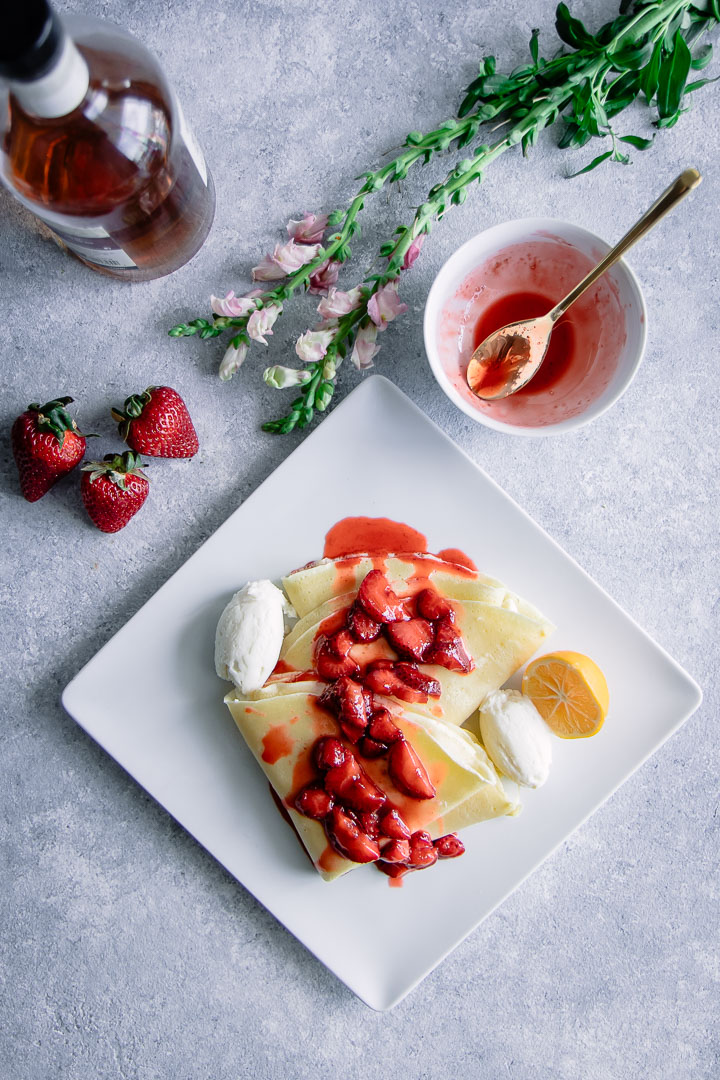 意大利乳清干酪和香草波旁草莓放在白色盘子里，蓝色的桌子上放着花。