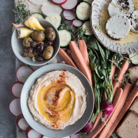 一甲板拼盘用白豆hummus，混合橄榄，纺织品，未加工的蔬菜和什锦饼干在蓝色的桌子上。