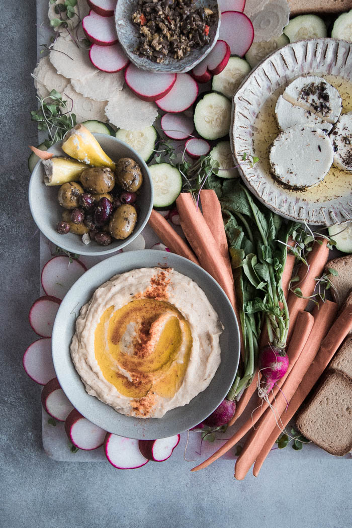 一甲板拼盘用白豆hummus，混合橄榄，纺织品，未加工的蔬菜和什锦饼干在蓝色的桌子上。