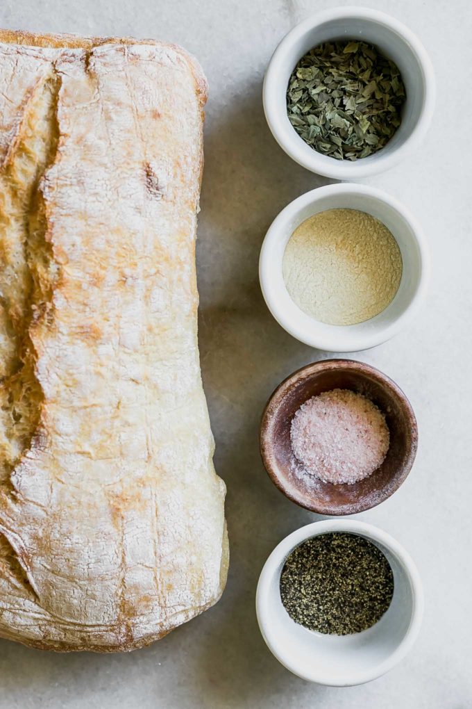 白色的桌子上放着意大利脆皮面包和几碗干香草、盐、胡椒和油
