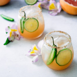 玛格丽塔酒用葡萄柚，石灰和桔子用在一张白色桌上的辣jalapenos与花。