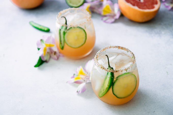 玛格丽塔酒用葡萄柚，石灰和桔子用在一张白色桌上的辣jalapenos与花。