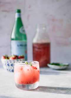 在一张蓝色桌上的草莓和薄荷的闪耀苏打水与一碗草莓和一个瓶苏打水在背景中。
