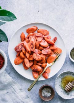 cooked carrots on a white plate with a gold fork and a side of honey and harissa sauce on a blue table