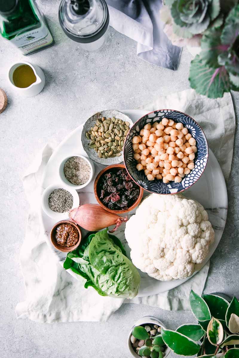 有碗的一块白色板材香料，鸡豆，蔓越桔，和种子在一张白色桌上与前面花椰菜和一瓶橄榄油