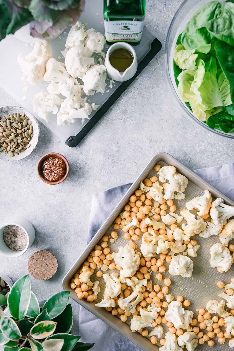 烤板用烤鸡豆和花椰菜在一张白色桌上与切板和一碗绿色莴苣