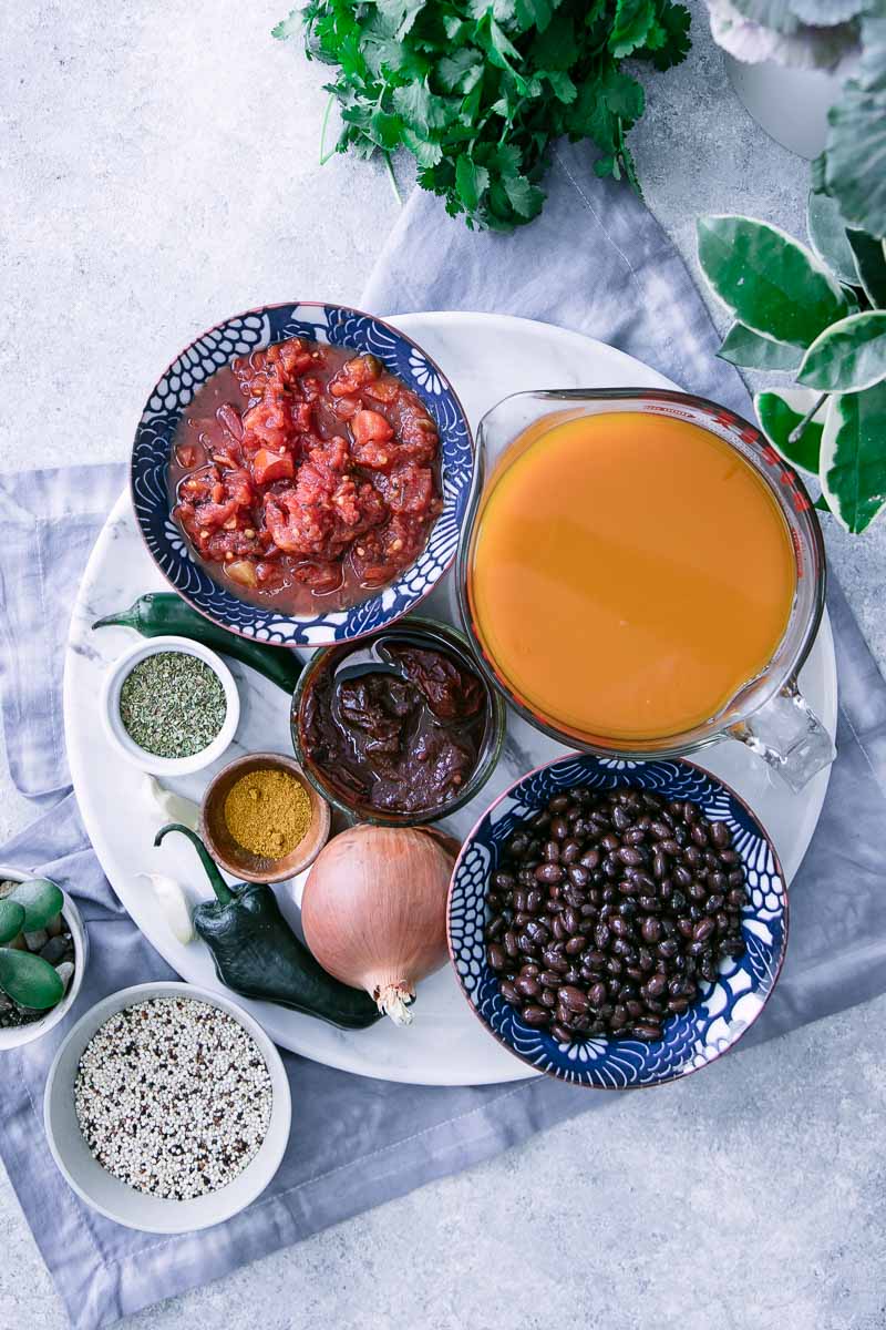 白色桌子上的小碗里盛着蔬菜汤、黑豆、烤西红柿、辣椒和香料