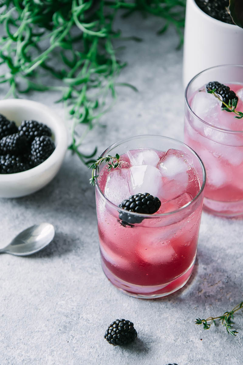 两杯加黑莓和百里香的苏打水加冰块放在桌子上，再放一碗黑莓