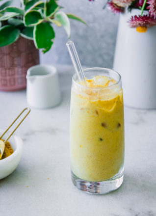 一杯与冰的黄金牛奶在一张蓝色桌用姜黄香料，花和素食主义者牛奶在背景中