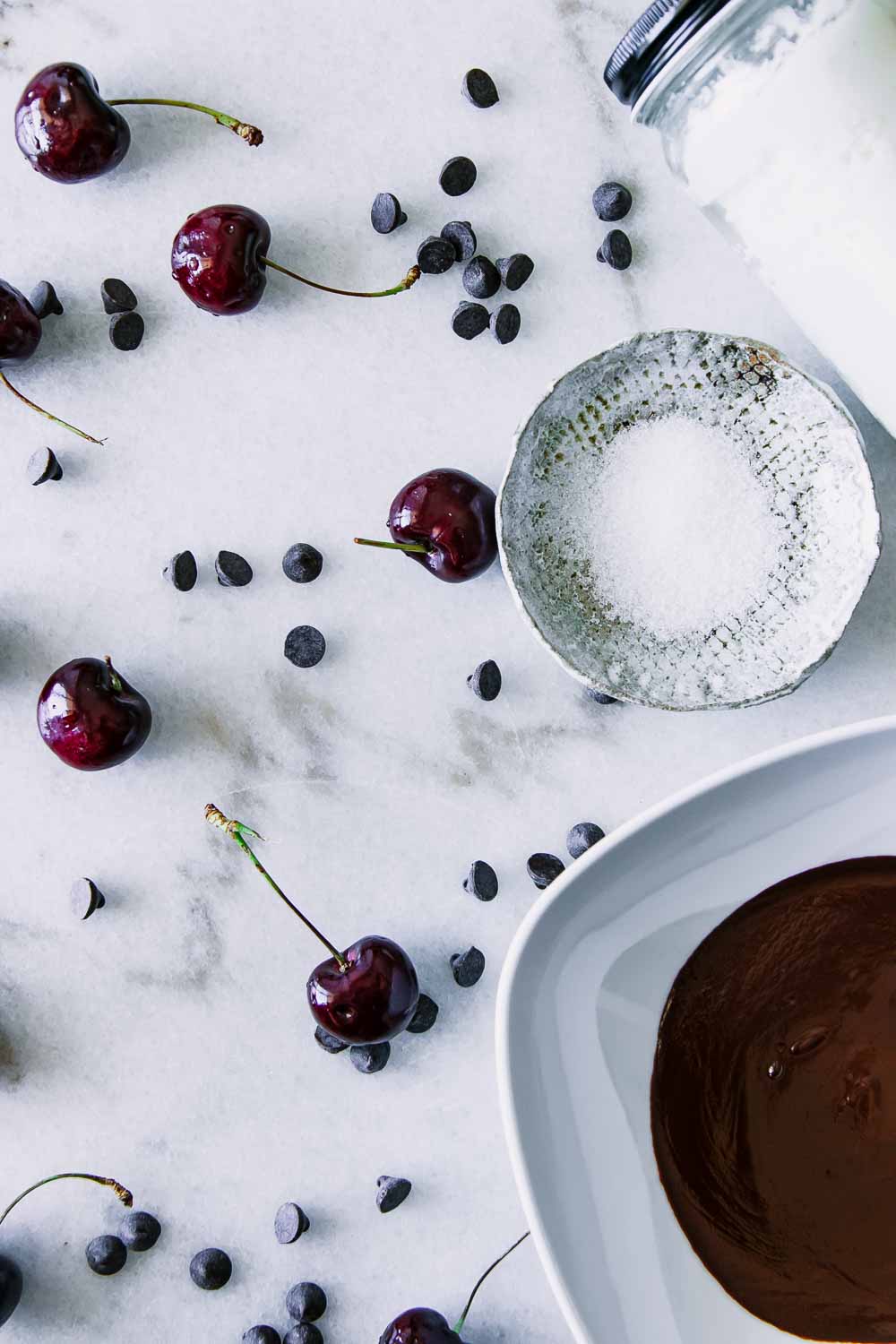 黑樱桃，黑巧克力片，一碗海盐，一碗融化的巧克力放在白色大理石桌上gydF4y2Ba