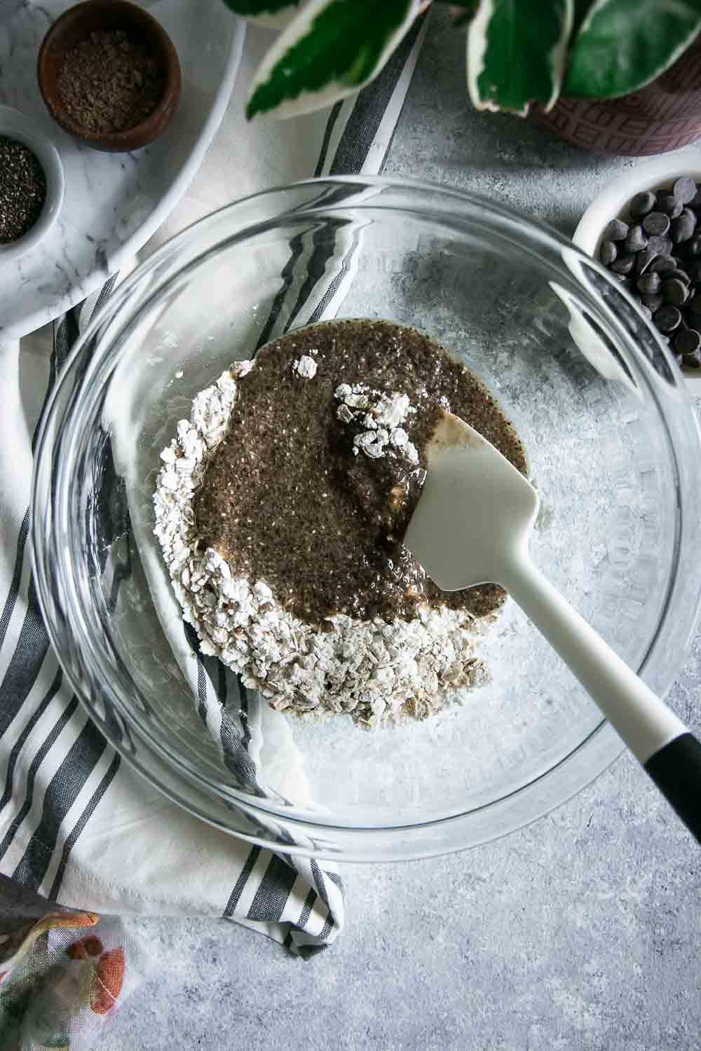 一个玻璃碗用干燥和湿燕麦粥巧克力曲奇饼和混合的匙子在一张灰色桌上