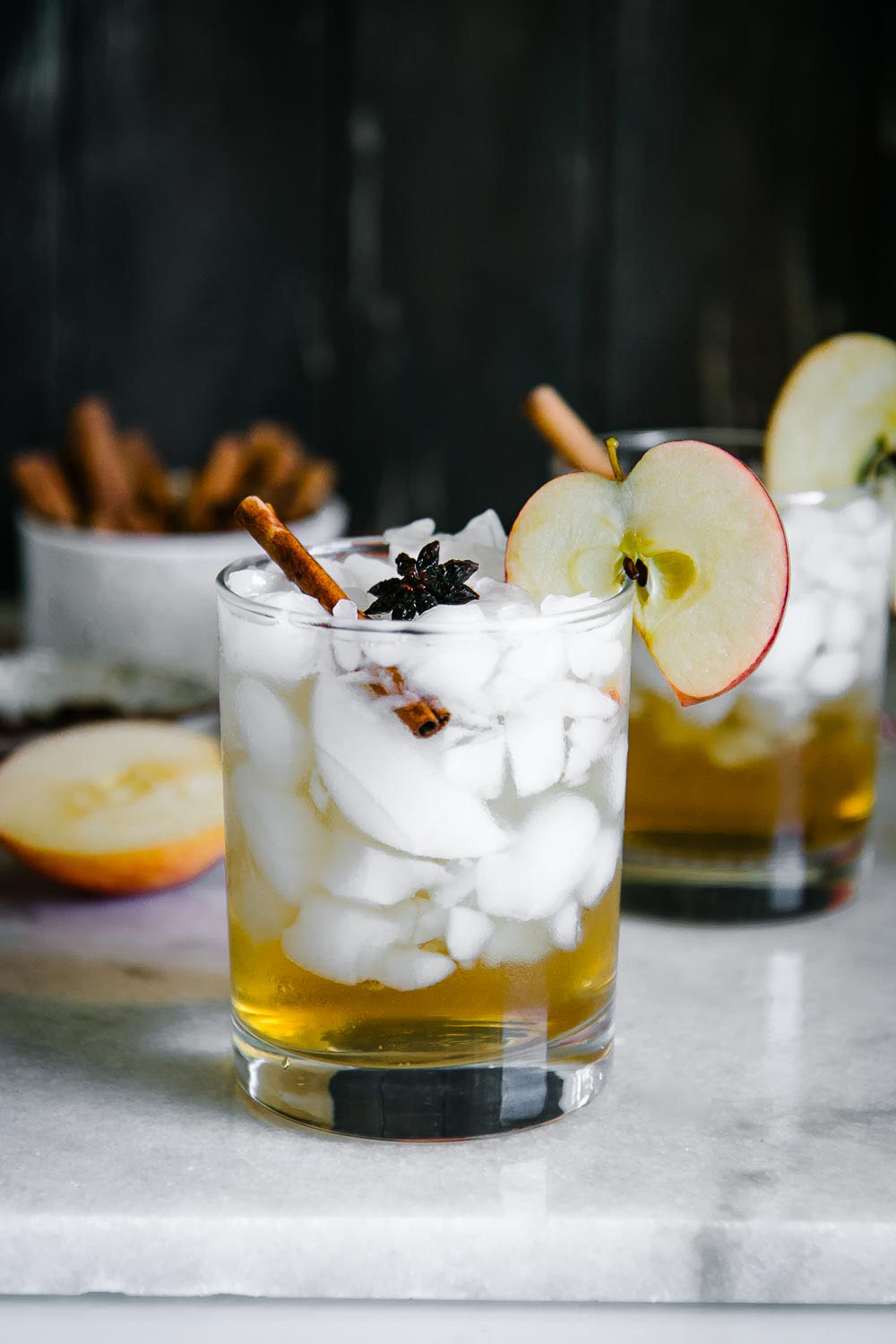与冰和苹果汁闪闪发光的鸡尾酒杯在一个白色大理石桌上的有黑背景