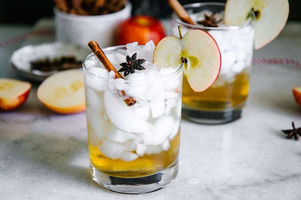 在冰的一个苹果汁醋闪闪发光在鸡尾酒玻璃用苹果切片和肉桂条在一张白色桌上装饰
