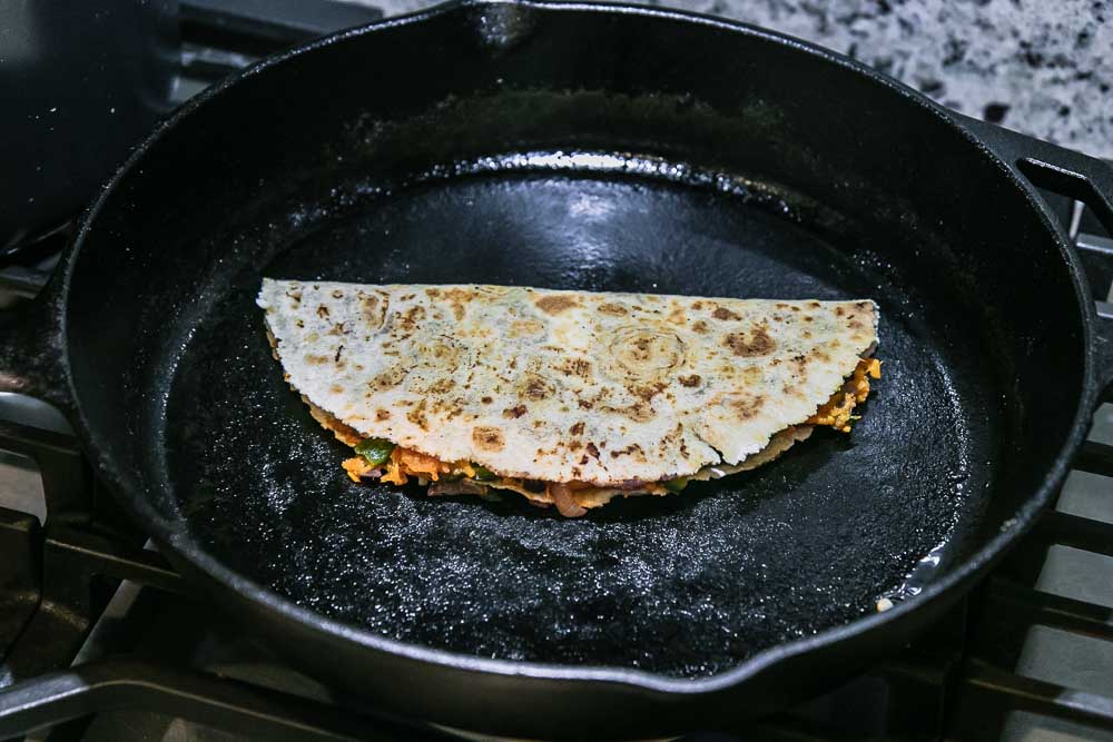 一块折叠的玉米饼，装满了甘薯和黑豆在炉灶上的黑色铸铁煎锅