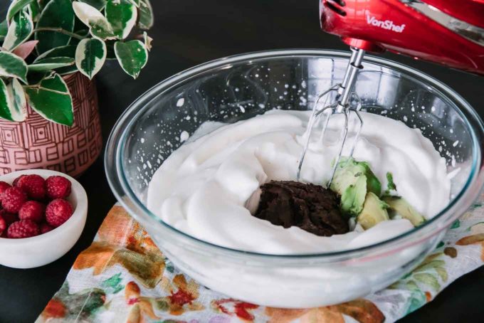 一个装有水椰汁，融化的巧克力，牛油果的碗，和一个红色的手持电动搅拌机