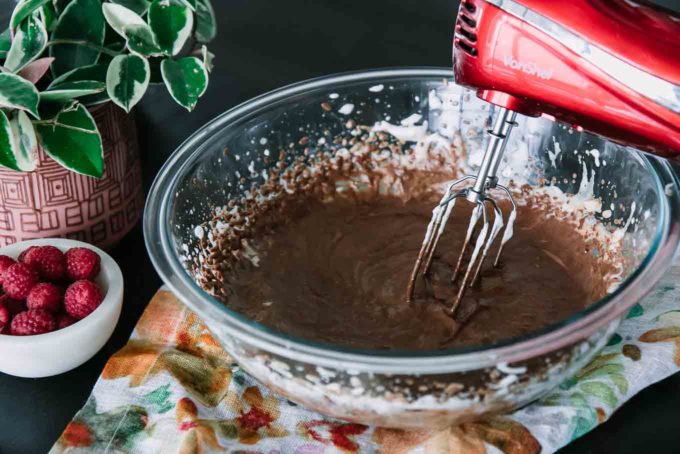 玻璃搅拌碗用混合的巧克力和在木桌上的红色手持式电动搅拌器