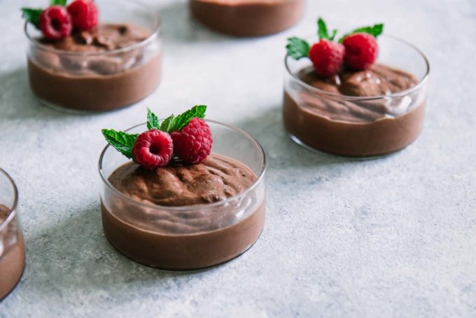小圆的玻璃碗巧克力奶油甜点用莓和薄菏在一张蓝色桌的上面