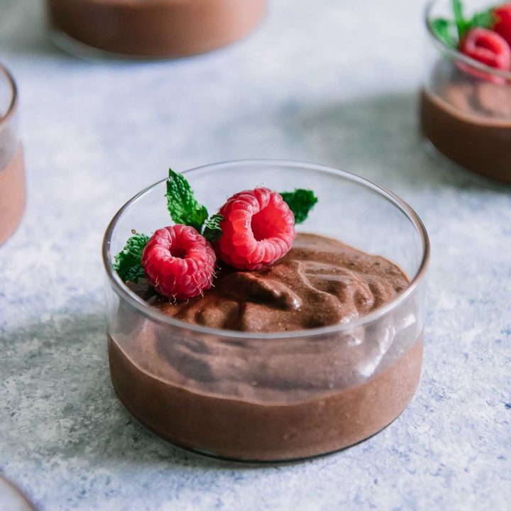 一个玻璃碗用棕色巧克力奶油甜点，红草莓和绿色薄荷小树枝在蓝色桌上