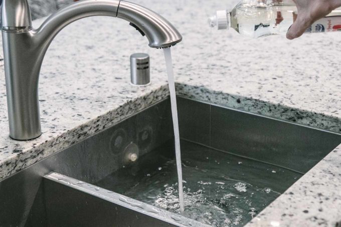 将洗碗皂倒入装满水的厨房水槽的手