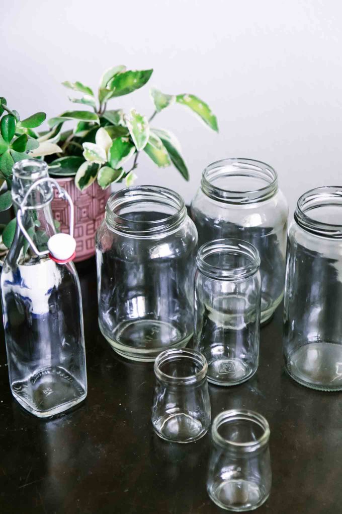 没有标签的空玻璃食品罐放在木桌上，背景是一株绿色植物