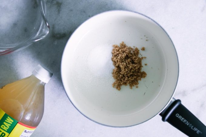 有盐和糖的小汁锅里面在一张白色桌上与一个测量的杯水和一瓶苹果醋