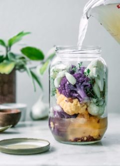 一罐白色、紫色和黄色的花椰菜，里面倒着醋汁