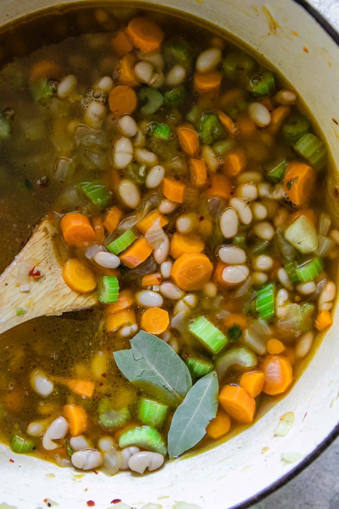 一个木勺搅拌蔬菜汤，胡萝卜和月桂在一个大汤锅