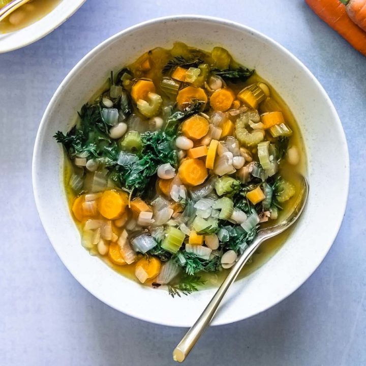 在蓝色的桌子上，白色的碗里有一碗蔬菜汤和绿叶胡萝卜