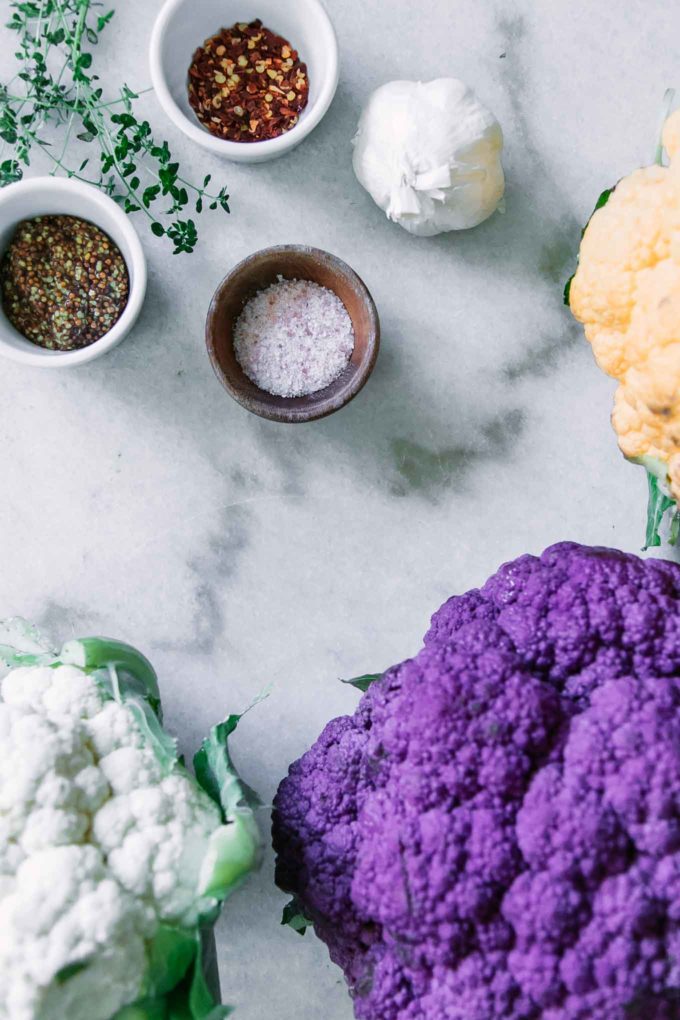花椰菜白色，紫色和黄色头在一张白色桌上的与三个小碗充满盐，芥末和红辣椒剥落