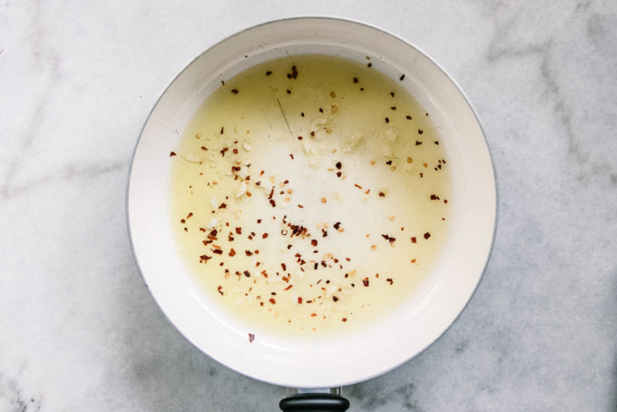 橄榄油，剁碎的大蒜和红辣椒剥落在白色桌上的白色平底锅