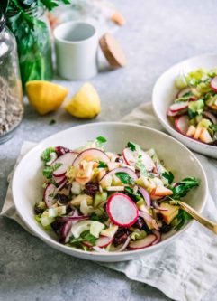 a colorful celery, apple, cranberry, and herb salad in a white bowl on a table with a white napkin