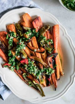 a white plate with roasted carrots and bell peppers on a white table with a blue napkin