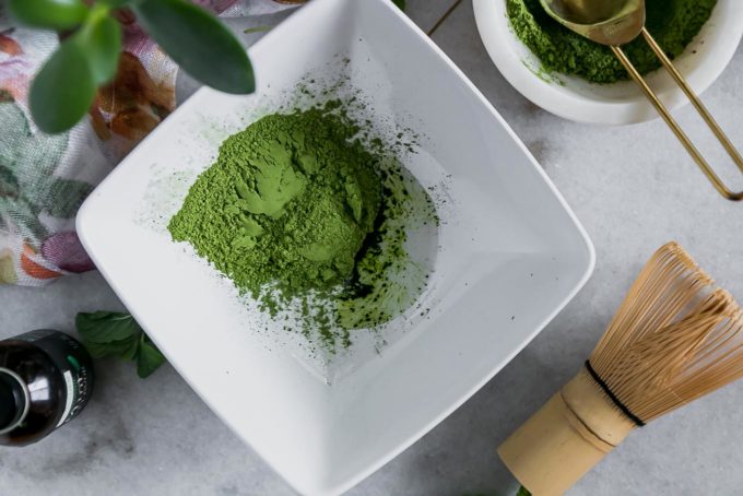 抹茶绿茶粉在一个碗里，薄荷提取物放在桌子上，一个木制的抹茶搅拌器