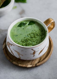 一杯绿茶抹茶拿铁，装在白色陶瓷马克杯里，放在木制茶托上