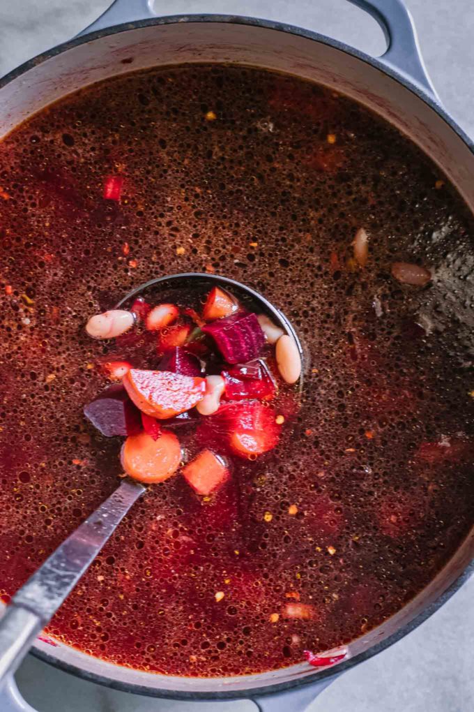在汤锅里混合红甜菜汤和蔬菜的勺子
